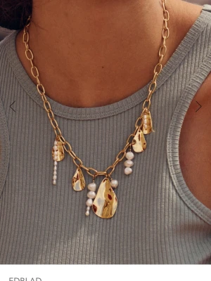 Guldhalsband med pärlor från Edblad - halsband Guldplaterad 14 k från Edblad med chunky guldfärgad kedja och flera droppformade hängen i metall samt vita pärlor. Halsbandet har en modern design med blandning av blanka metaller och pärldetaljer som ger en cool och trendig look.