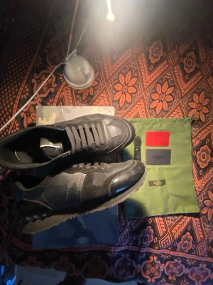Valentino Rockrunners  - Säljer ett par svarta sneakers med snygga mockadetaljer och klassisk låg siluett. Skorna har svarta skosnören, gummisula och diskreta sömmar som ger en stilren look. Perfekta för dig som gillar streetwear och vill ha något som funkar till det mesta.