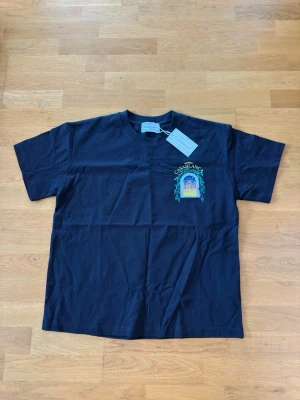 Svart t-shirt från Casablanca - Svart t-shirt från Casablanca med färgglatt tryck på bröstet där det står 'Avenida Casablanca' och ett motiv av en byggnad. Klassisk passform och rund hals. Perfekt för dig som vill ha en stilren men ändå unik look.