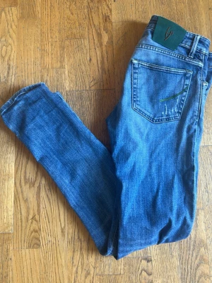 Handpicked jeans slim fit - Snygga blå skinny jeans med slitningar och en unik grön detalj på bakfickan. Jeansen har klassisk femficksdesign och smal passform. Perfekta för dig som gillar en avslappnad och trendig stil. Priset är ej hugget i sten så om ni har några frågor elr rimliga bud är det bara att kontakta
