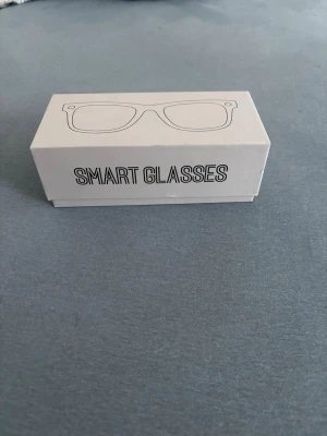 Svarta smarta glasögon -  Spelar in videos och tar bilder Säljer ett par svarta smarta glasögon med klassisk design. Medföljer brunt fodral, extra linser och putsduk. Glasögonen har robust plastbåge och passar perfekt för dig som vill ha teknik och stil i ett.