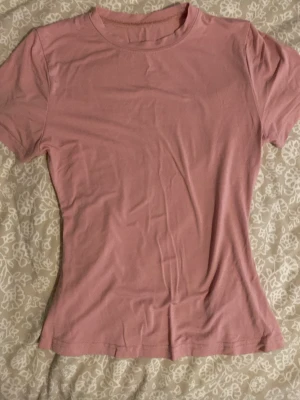 Rosa tränings t-shirt - Enkel och stilren rosa tränings t-shirt med rund hals och korta ärmar. Modellen är figursydd och passar perfekt till träning eller vardagsaktiviteter. Tillverkad i mjukt och stretchigt material för skön passform.