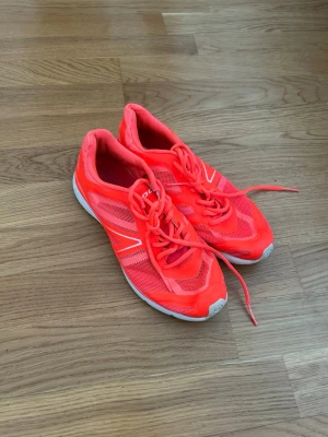 Neonröda sneakers med vita detaljer - Snygga sneakers i neonrött med vita detaljer och snörning. Skorna har en sportig design med meshpaneler för extra ventilation och en vit sula som ger bra grepp. Perfekta för dig som gillar färgstarka skor och vill sticka ut.