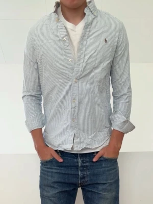 Ljusblå Randig Ralph Lauren skjorta  - Ljusblå Randig Ralph Lauren skjorta i barnstorlek 16 vilket motsvarar och sitter som en S! Bra skick utan nåra defekter och hör gärna av er vid frågor elr funderingar!!