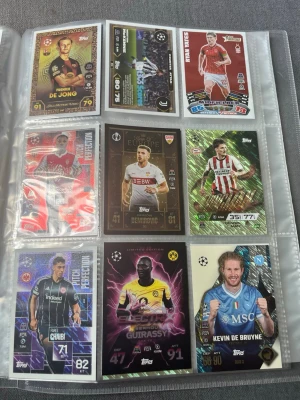Fotbollskort Topps samling i pärm - Samling med fotbollskort från Topps i plastfickor i en pärm. Korten har färgstarka designer, holografiska effekter och motiv av kända spelare från olika europeiska klubbar. Finns 109 kort i denna pärm, hör av dig för att se resten av korten då jag inte hade plats att fota alla, pris kan ändras vid snabb affär, går även att köpa enskilda kort