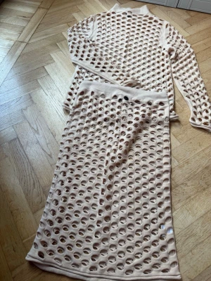Oanvänd Beige långärmad hålmönstrad topp och kjol, st S - Garderob rensning! St M. Aldrig använt. Trendig beige långärmad topp i 100% bomull med stort hålmönster över hela plagget. Toppen har rund hals och är perfekt för lager på lager-stil. Matcha med kjol som är knälång. Setet - inspirerad av italiensk märkes  sett Max M##a 