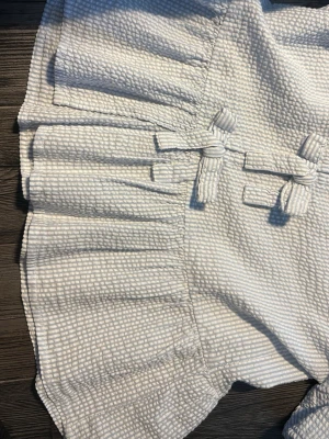 Ljus blå blus  med knyt och struktur - Supersöt ljus blå blus  med strukturerat tyg och flera dekorativa knyt framtill. Blusen  volangdetaljer nedtill och ett unikt mönster i tyget som ger en modern känsla. Perfekt för dig som gillar detaljer och en feminin look.