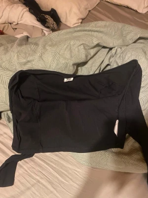 Svart omlott topp med knyt - Trendig svart omlott kofta med knyt i sidan. Koftan är croppad och har en axelbandslös design som ger en snygg och modern look. 