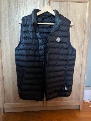 Moncler väst - Snygg svart dunväst från Moncler med quiltad design och hög krage. Västen har två dragkedjefickor framtill och Moncler-logga på bröstet. Perfekt för lager-på-lager och håller dig varm under kyliga dagar. Ni vet varför lågt pris‼️