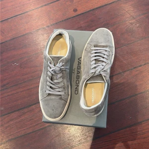 Gråa sneakers från Vagabond - Snygga gråa sneakers från Vagabond i mocka med klassisk låg profil och vita sulor. Skorna har matchande grå skosnören och en stilren design som passar till det mesta. Perfekta för dig som gillar en clean och enkel look.
