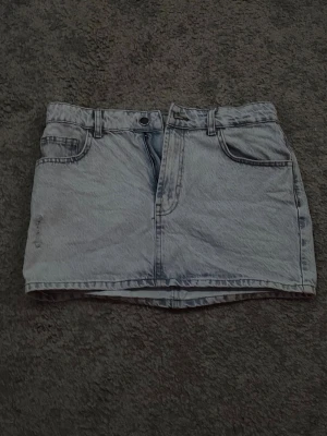 Ljusblå jeanskjol med fickor - Trendig ljusblå jeanskjol i kort modell med klassiska fickor fram och bälteshällor. Kjolen har knapp och dragkedja framtill och är perfekt för en avslappnad stil.