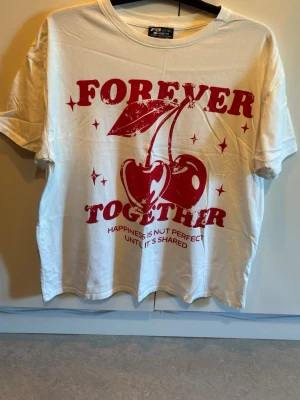 Vit t-shirt med körsbär från FB Sister - Vit loose fit t-shirt från FB Sister med stort rött tryck framtill som visar körsbär och texten 'Forever Together'. Skön och avslappnad passform, perfekt till jeans eller shorts. Tillverkad i mjuk bomull.
