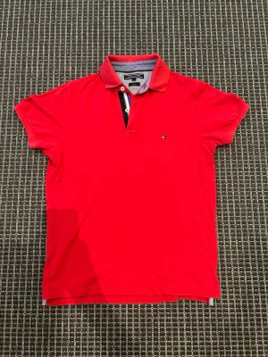 Röd pikétröja Tommy Hilfiger - Snygg röd pikétröja från Tommy Hilfiger med klassisk krage och knappslå med blå och vita detaljer. Slim fit-modell som ger en modern siluett. Liten logga på bröstet och kontrastfärg på insidan av kragen.