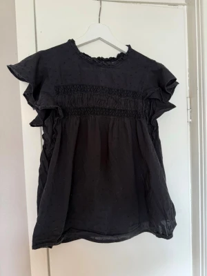 Svart blus med volangärmar - Snygg svart blus med volangärmar och smockdetaljer över bröstet.  Den har små fläckar som inte är så tydliga men därav priset. Den är från vero Moda och i storlek xs. Pris kan diskuteras!