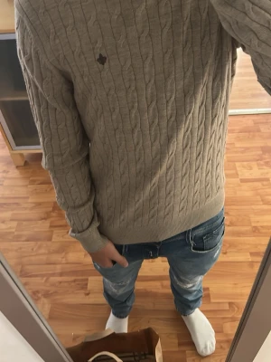 Beige stickad tröja - Snygg beige stickad tröja med rund hals och diskret emblem på bröstet. Tröjan har långa ärmar och ribbade muddar vid ärmslut och nederkant. Perfekt för lager på lager och enkel att matcha med jeans. Nypris 1299kr.