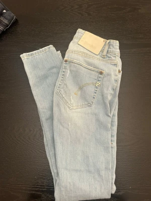 Ljusblå dondup jeans med slitningar och  med raka ben - Säljer ett par ljusblå jeans från dondup med raka ben och slitningar på framsidan. Jeansen har klassisk femficksdesign och är gjorda i denim. Perfekta för en avslappnad och trendig look.
