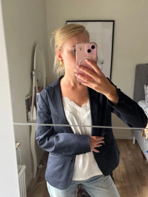 Mörkblå klassisk kavaj - Snygg mörkblå kavaj med två knappar framtill och klassisk krage. Kavajen har två fickor med lock och en bröstficka. Passformen är rak och materialet ser ut att vara en blandning av bomull och polyester. Perfekt att styla med jeans eller kjol.