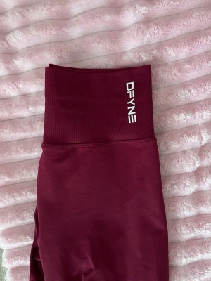 Vinröda leggings från DFYNE - Säljer ett par vinröda leggings- kollektion Dynamic från DFYNE. De har en tight passform och är perfekta för gymmet. Materialet är stretchigt och följsamt för maximal komfort. Loggan sitter på linningen framtill. Använda kanske 3 gånger, säljer då jag tycker midjan är för hög för min smak🫣 en liten defekt på sömnen längts ner vid ankeln som syns på sista bilden, dock inget hål på tightsen. Priset som syns är vad som gäller🙏🎀😗💕