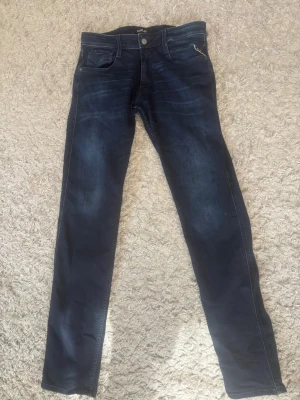 Mörkblå slim fit jeans från Replay - Snygga mörkblå slim fit jeans från Replay med klassisk femficksdesign och subtila slitningar. Jeansen har en skinnpatch med Replay-logga bak i midjan och kontrastsömmar. Perfekta för dig som gillar en smal siluett och tidlös stil.