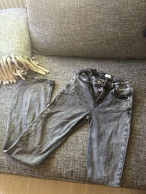 Grå tvättade flare/bootcut jeans - Säljer ett par grå tvättade jeans med klassisk femficksdesign. Jeansen har knappgylf och bälteshällor i midjan. Märket är Grunt köpta från kidsbeandstore💕