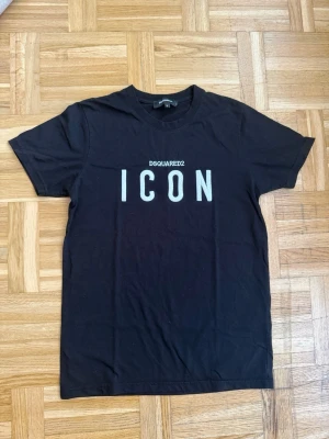 Svart ICON t-shirt från Dsquared2 - Snygg svart t-shirt från Dsquared2 med stort vitt 'ICON'-tryck på bröstet. Klassisk rund halsringning och korta ärmar. Tillverkad i mjuk bomull som känns skön mot huden. Perfekt för dig som gillar stilrena statement-plagg. Storlek S-M. Använd