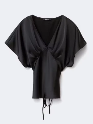 Svart omlottopp i satin - Snygg svart omlottopp i satin med v-ringning och korta, vida ärmar. Toppen har knytband i midjan för en justerbar passform och en elegant, glansig finish. Perfekt att styla med jeans eller kjol för en trendig look.