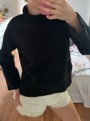 Svart stickad tröja med polokrage - En fin svart stickad tröja perfekt till hösten. Varm och har ribbat mönster runt halsen, långt ner vid magen och längst ner vid ärmarna. 