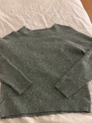 Grön stickad tröja med rund hals - Mysig grön stickad tröja med rund hals och långa ärmar. Tröjan har ribbstickade muddar vid ärmslut och nederkant, vilket ger en klassisk och enkel look. Perfekt för kyliga dagar och lätt att matcha med olika outfits.