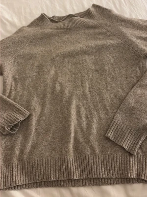 Beige stickad tröja med rund hals - Mysig beige brun stickad tröja med rund hals och ribbade muddar vid ärmslut och nederkant. Tröjan har en enkel och stilren design som passar perfekt till lager på lager. Materialet ser ut att vara mjukt och skönt, perfekt för kyligare dagar.