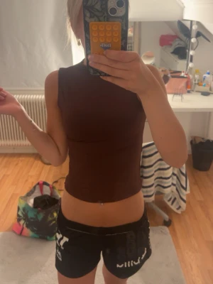 Brun ärmlös croppad topp - Säljer en brun, tight och croppad topp utan ärmar. Toppen har en enkel och stilren design med hög halsringning och är tillverkad i ett stretchigt material som sitter snyggt mot kroppen. Perfekt att matcha med jeans eller kjol.