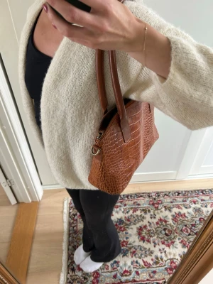 Brun handväska i ormmönstrat skinn - Snygg brun handväska från Manfield i ormmönstrat skinn. Väskan har två handtag, guldfärgade detaljer och dragkedja upptill. Insidan är fodrad och rymlig! Super snygg!