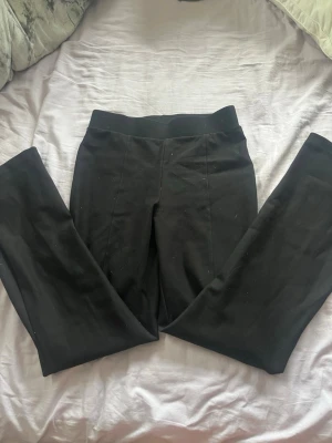 Svarta leggings med hög midja - Säljer ett par svarta leggings med hög midja och bred resår i midjan. De har en stilren look med söm framtill och fejkade fickor bak. Materialet är stretchigt och mjukt, perfekt för en bekväm och snygg outfit.