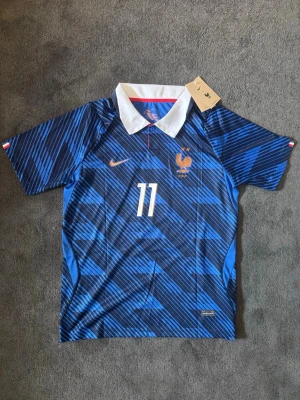 Frankrike VM 26/27 hemma Olise 11 - Tröjan är helt ny med tagg kvar och i perfekt skick. Storlek M. Perfekt för dig som är supporter, samlar på fotbollströjor eller vill ha en snygg tröja till träning och vardag. 🔹 Storlek M 🔹 Helt ny med tagg 🔹 Olise 🔹 Skickas inom 24 timmar Vid intresse eller frågor är det bara att skicka