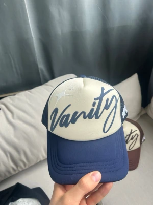 Trucker Keps - Puffprint o framsidan och embroidery text på sidan av kepsen, navy och kräm vit färg