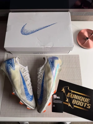 Nike Mercurial Vapor 16 Blueprint - Säljer ett par Nike Mercurial Vapor 16 fotbollsskor i vitt och blått med orange detaljer. Skorna är limiterat tillverkade och säljs vidare för 5000sek+, köpta på EuniqueBoots så självklart äkta. Storlek 44= 27cm sula. Använda i bara någon månad så i väldigt fint skick