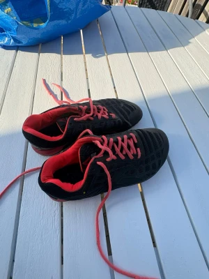 Svarta Reebok sneakers med röda detaljer - Säljer ett par svarta Reebok sneakers med mesh-överdel och röda innersulor samt röda skosnören. Skorna har en sportig look med låg profil och ventilerande material, perfekta för dig som gillar streetstyle och komfort.