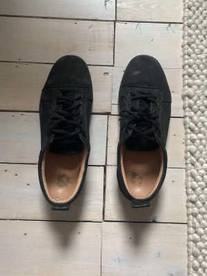 Svarta sneakers från Christian Louboutin - Snygga svarta sneakers från Christian Louboutin i mocka med klassiska röda sulor och svarta skosnören. Låg modell med stilren design och diskreta sömmar. Perfekta för dig som vill ha något exklusivt och tidlöst i garderoben. Kan gå ner vid snabb affär 👌