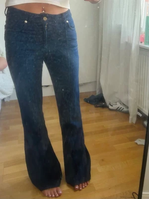 Mörkblå utsvängda jeans - Säljer ett par mörkblå jeans med hög midja och utsvängda ben. Jeansen har klassiska fickor fram och bak, samt synliga sömmar längs benen. Perfekta för dig som gillar retrostil och vill ha ett par riktigt snygga jeans i garderoben.