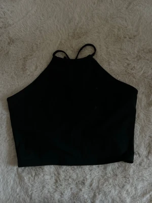 Svart  halterneck topp - Snygg svart halterneck topp med tunna axelband och öppen rygg med snörningsdetaljer. Mjukt och stretchigt material. Storlek xs 
