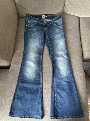 Blå utsvängda jeans från 157 - Säljer ett par blå jeans från 157 med utsvängda ben och slitna detaljer framtill. Klassisk femficksmodell och låg midja. Perfekta för dig som gillar retrovibbar och vill ha ett par riktigt snygga jeans med cool tvätt.