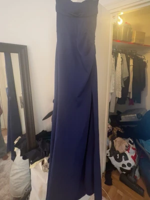 Marinblå balklänning med slits - Elegant marinblå långklänning med figurnära passform och axelbandslös design. Klänningen har en markerad midja och en hög slits framtill som ger en snygg siluett. Perfekt för bal eller festliga tillfällen.