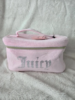 Rosa necessär från Juicy Couture - Söt rosa necessär i mjuk velour från Juicy Couture med glittrande Juicy-text framtill. Väskan har guldfärgade dragkedjor och detaljer samt ett praktiskt handtag upptill. Perfekt för smink eller småprylar när du är på språng.