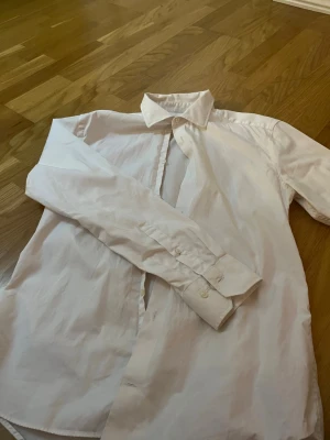Vit slim fit skjorta från Riley - Klassisk vit skjorta från Riley i slim fit-modell. Skjortan har långa ärmar, knappar framtill och vid ärmsluten samt en stilren krage. Perfekt för dig som gillar en enkel och clean look.