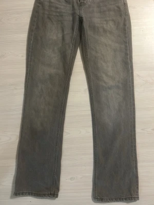 Grå raka jeans - Säljer ett par grå jeans med rak passform och klassisk femficksdesign. Jeansen har normal midja och är tillverkade i ett mjukt denimtyg. Perfekta för en avslappnad och stilren look.