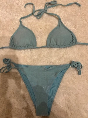 Ljusblå glittrig bikini med knyt - Supersnygg ljusblå bikini med glittrigt tyg. Klassisk trekantsmodell upptill och knyt i sidorna på underdelen🌸