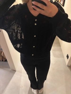 Svart transparent kofta med pärlknappar - Snygg svart kofta med transparent, stickad struktur och dekorativa pärlknappar framtill. Koftan har v-ringning, lång ärm och en lite lösare passform🌸