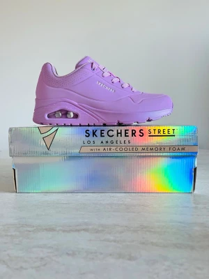Lila Skechers Uno sneakers - Snygga lila Skechers sneakers med chunky sula och synlig luftdämpning i hälen. Skorna har air-cooled memory foam för extra komfort och är tillverkade i syntetmaterial. Perfekt för dig som vill sticka ut med färg och stil.