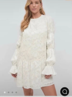 Vit miniklänning med puffärm - Supersöt vit miniklänning med blommigt mönster, voluminösa puffärmar och breda volangslut. Klänningen har rund halsringning fram och djup rygg med knytband. Tillverkad i ett lätt, transparent tyg med romantisk känsla. Från Gina tricot, Stl 32! Använd 1 gång.