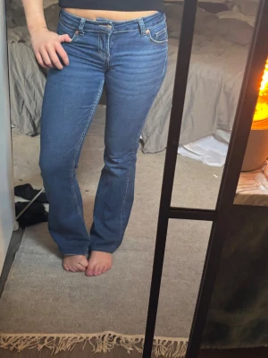 Blå bootcut jeans med stretch - Säljer ett par klassiska blå bootcut jeans med stretchig passform och Lågmidja. Jeansen har fem fickor, bälteshällor och stängs med dragkedja och knapp. Perfekta för dig som gillar en tidlös look med lite utsvängda ben. Jag har sytt upp dem så dem passar mig som är 167