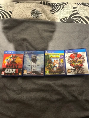 PS4 spelpaket: Red Dead, Star Wars, Crash, Street Fighter - Säljer fyra PS4-spel: Red Dead Redemption II, Star Wars Battlefront, Crash Bandicoot N. Sane Trilogy och Street Fighter V. Alla spel kommer i sina original blå plastfodral med färgglada omslag. Perfekt för dig som gillar action, äventyr och fighting!